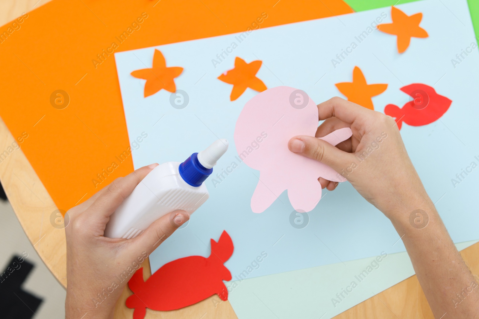 Photo of Girl applying glue onto paper figure for her creative project at table indoors, closeup. Art and craft