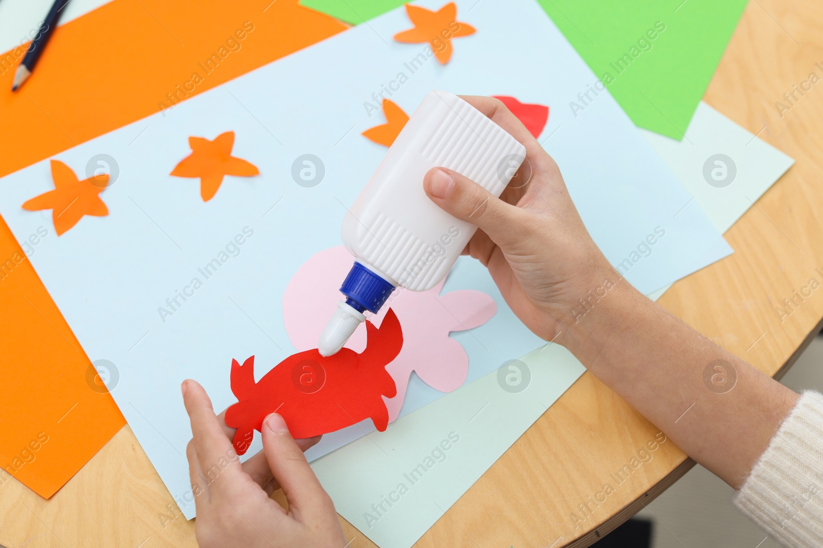 Photo of Girl applying glue onto paper figure for her creative project at table indoors, closeup. Art and craft