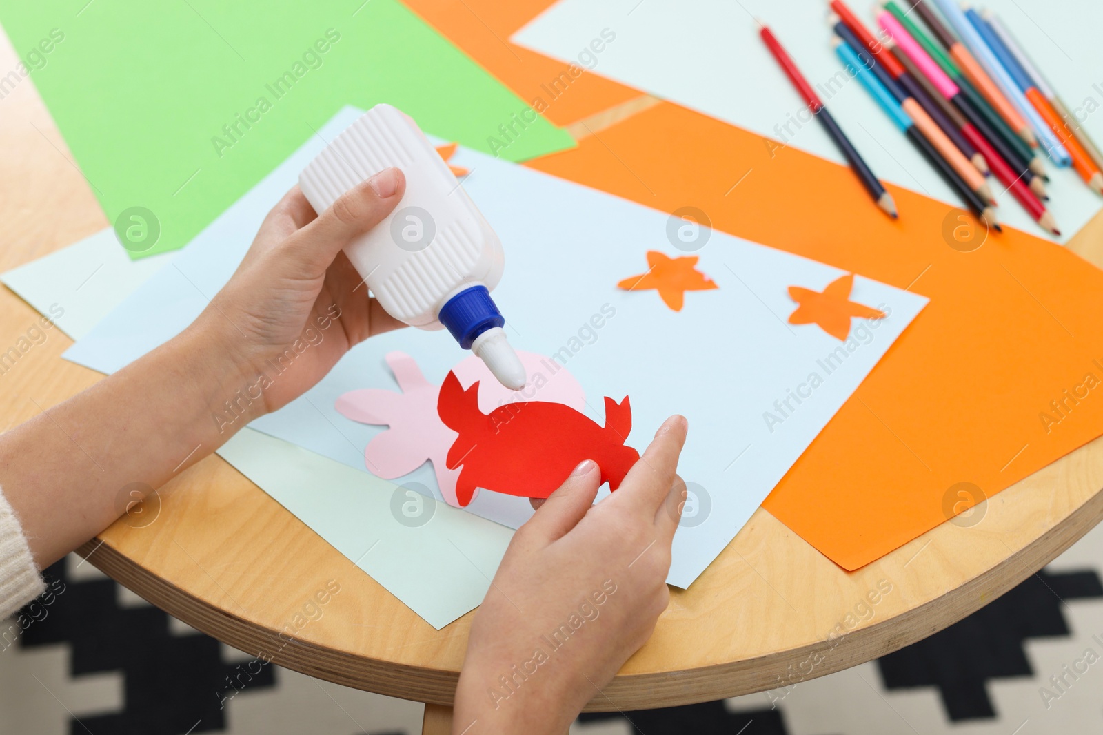 Photo of Girl applying glue onto paper figure for her creative project at table indoors, closeup. Art and craft