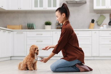 Photo of Smiling owner feeding her cute dog with dry pet food in kitchen