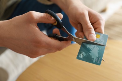 Photo of Man cutting credit card at wooden table indoors, closeup