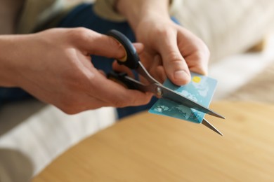 Photo of Man cutting credit card at wooden table indoors, closeup