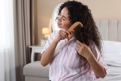 Photo of Smiling young woman brushing her curly hair with comb at home