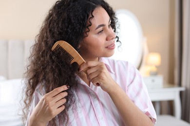 Photo of Beautiful young woman brushing her curly hair with comb at home