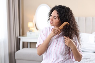 Photo of Smiling young woman brushing her curly hair with comb at home