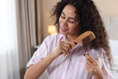 Smiling young woman brushing her curly hair with comb at home