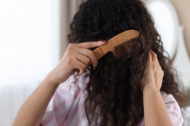 Photo of Woman brushing her curly hair with comb at home