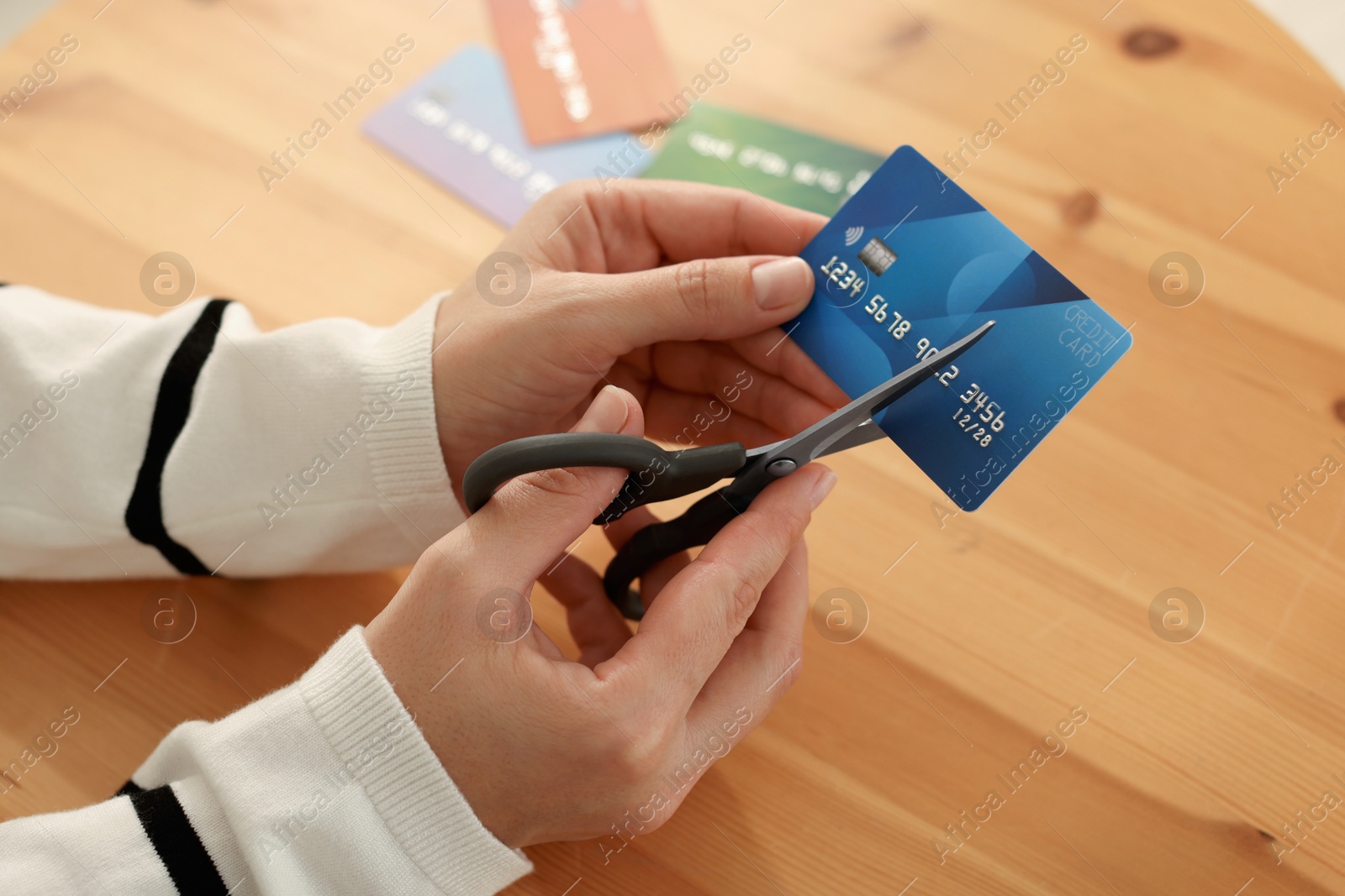 Photo of Woman cutting credit card at wooden table indoors, closeup