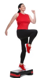 Photo of Plus size woman in gym clothes doing exercise with step platform on white background