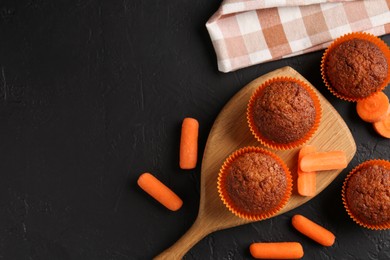 Photo of Delicious carrot muffins with fresh vegetables on black table, flat lay. Space for text