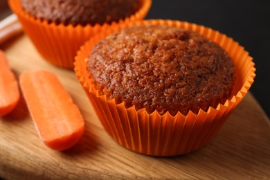 Photo of Tasty carrot muffins with fresh vegetable on black table, closeup