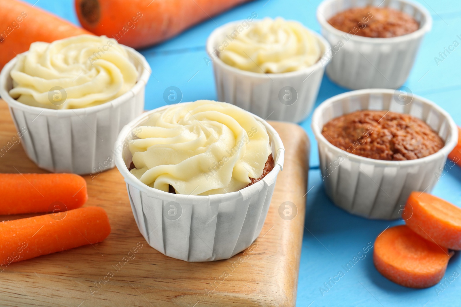 Photo of Tasty carrot muffins with fresh vegetables on light blue wooden table, closeup