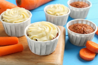 Photo of Tasty carrot muffins with fresh vegetables on light blue wooden table, closeup