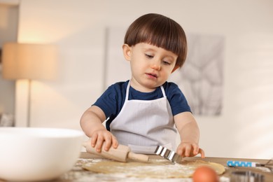 Photo of Cute little boy with rolling pin and cookie cutter at table indoors