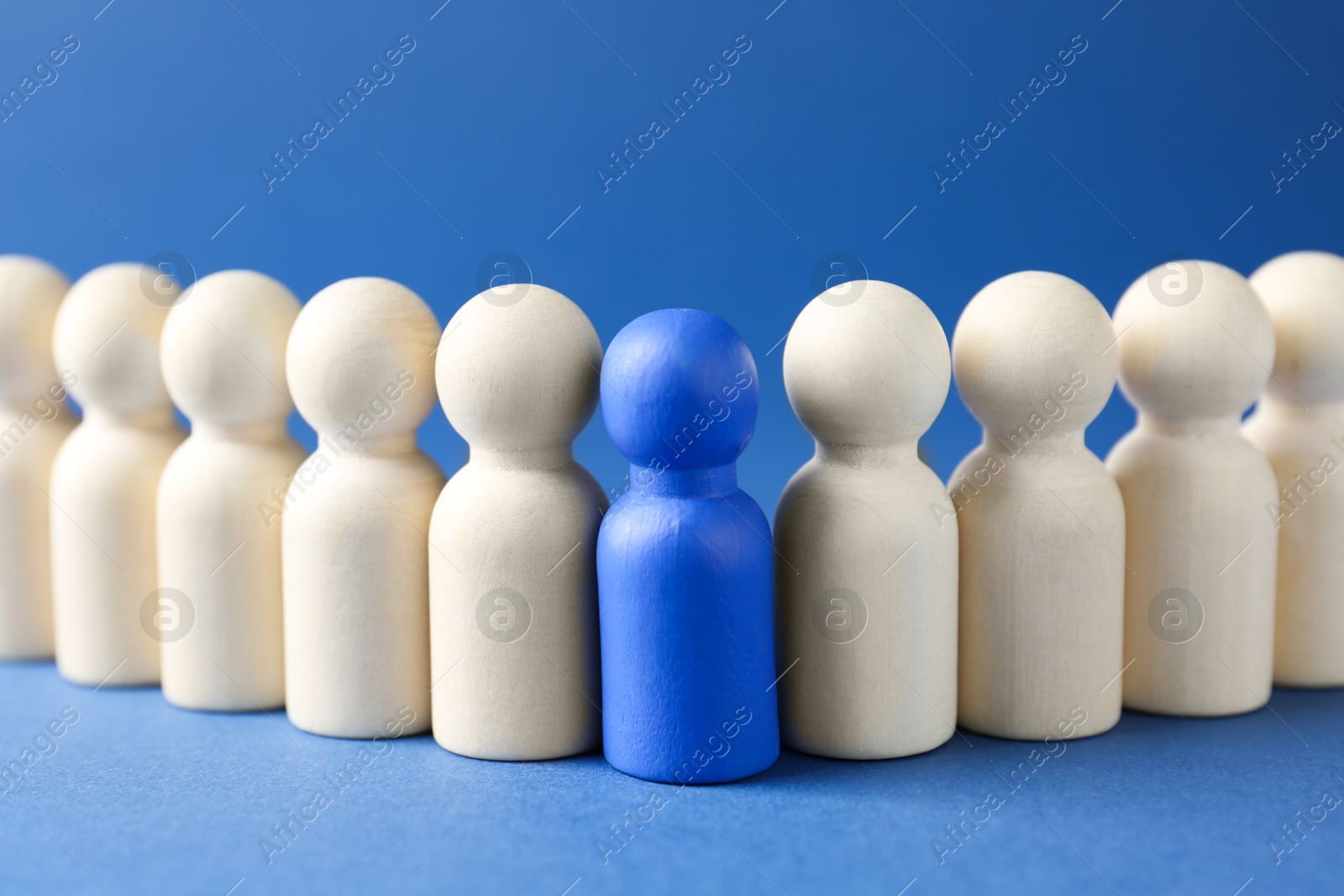 Photo of Competition concept. Color human figure among wooden ones on blue background, closeup