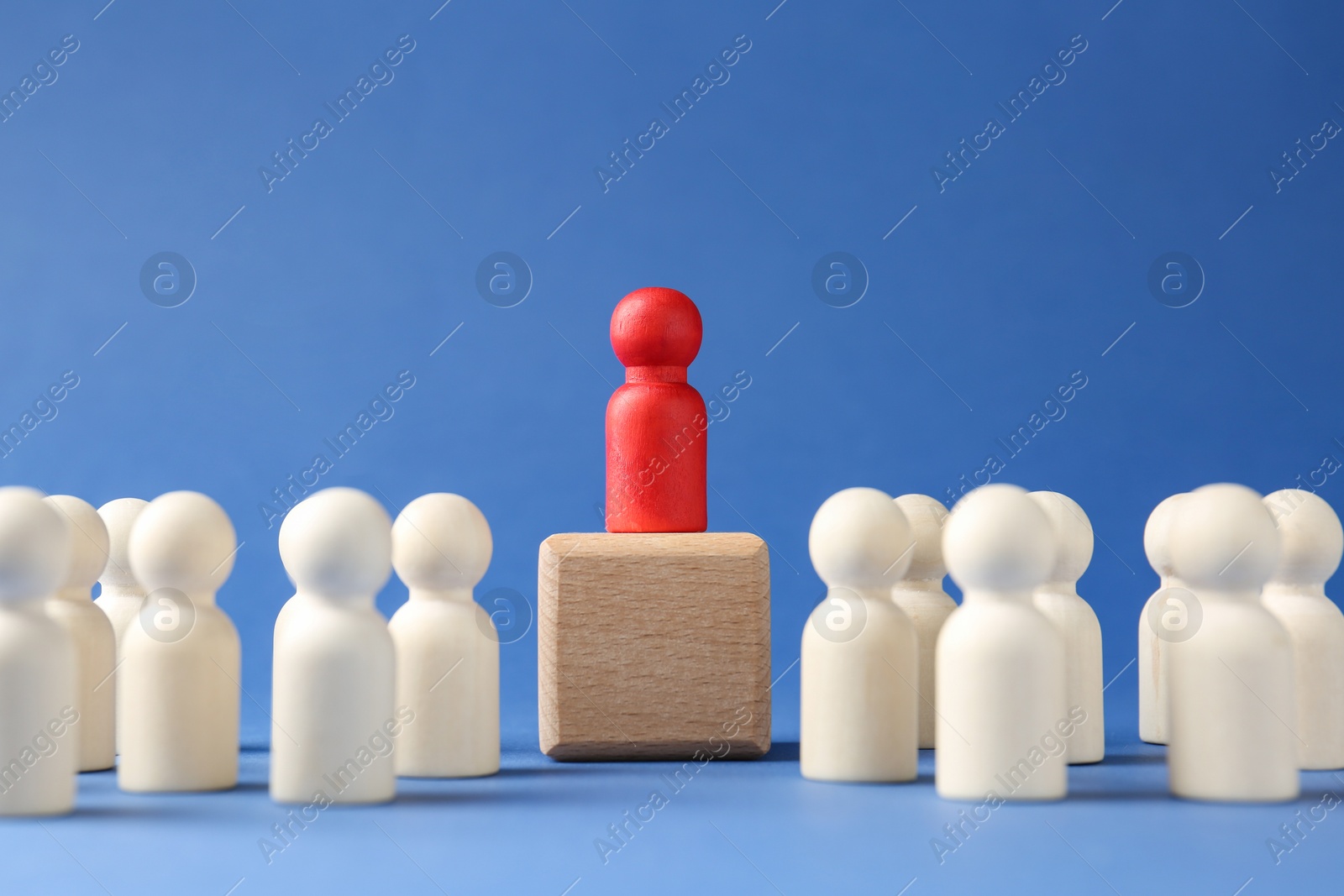 Photo of Competition concept. Human figure on wooden cube and other ones behind against blue background