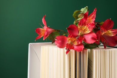 Book and beautiful alstroemeria flowers on green background, closeup. Space for text