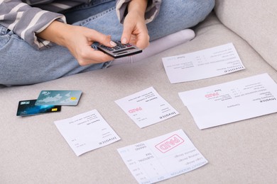 Photo of Paying bills. Woman with different invoices, credit cards and calculator on couch at home, closeup