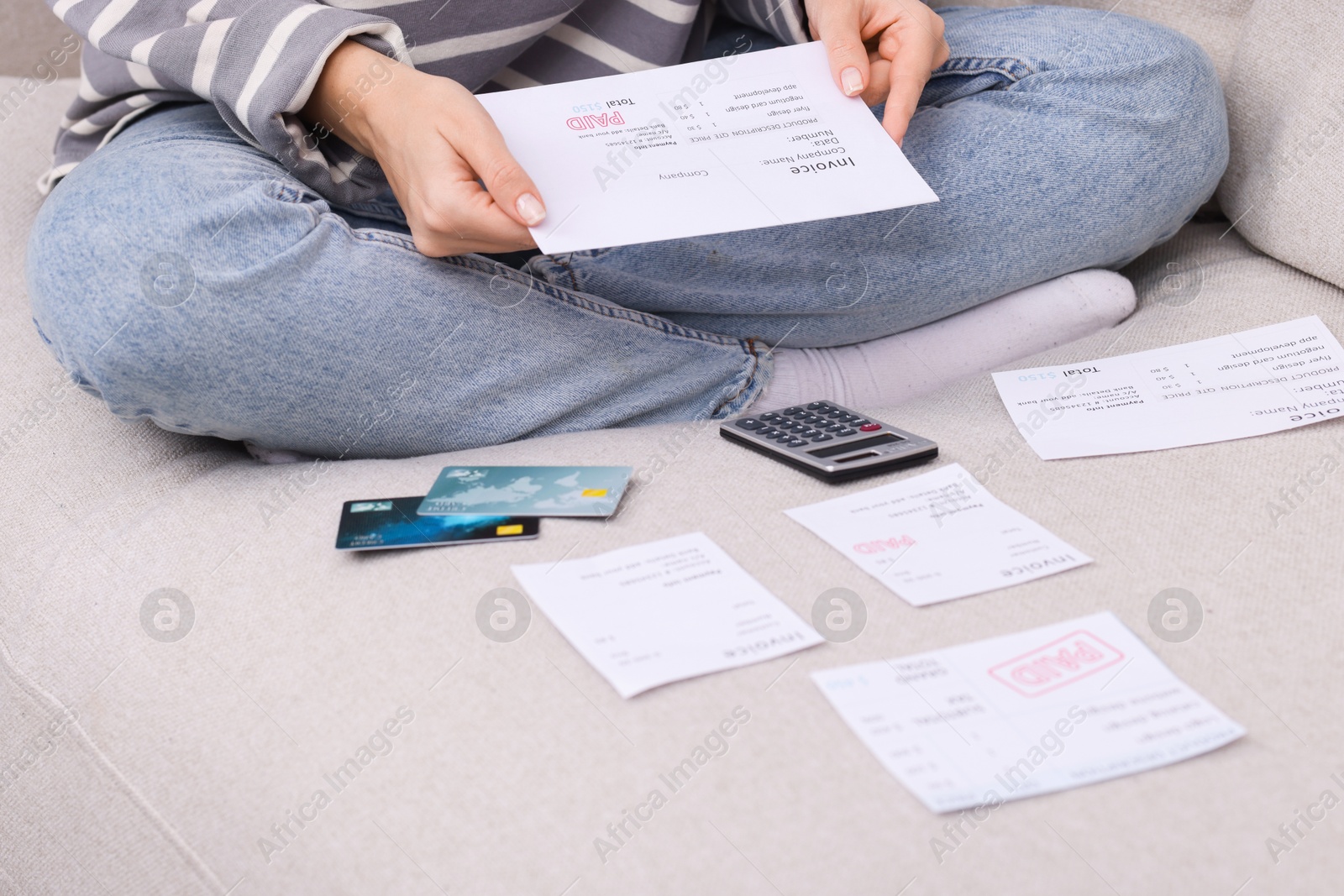 Photo of Paying bills. Woman with different invoices, credit cards and calculator on couch at home, closeup