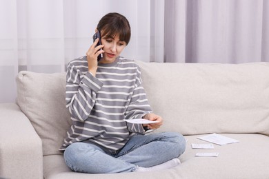 Paying bills. Woman with different invoices talking on phone on couch at home, space for text