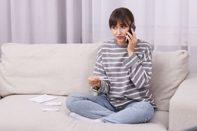 Photo of Paying bills. Woman with different invoices talking on phone on couch at home, space for text