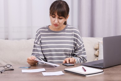 Photo of Paying bills. Woman with different invoices and calculator at wooden table indoors