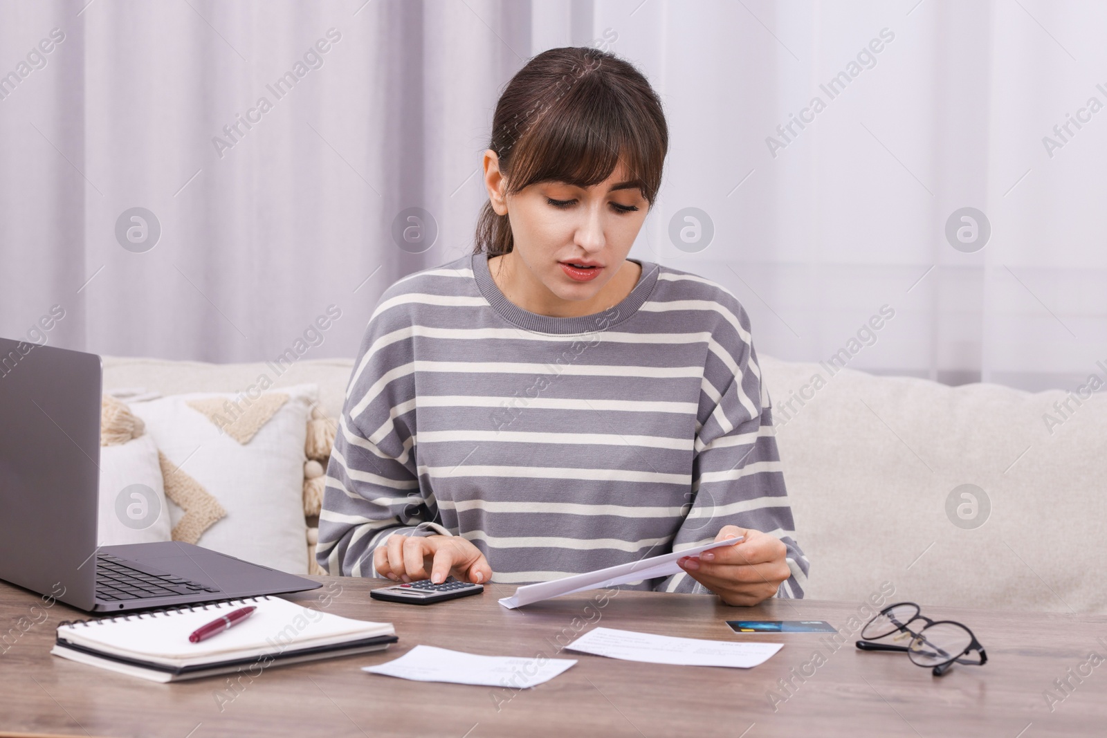 Photo of Paying bills. Woman with different invoices and calculator at wooden table indoors