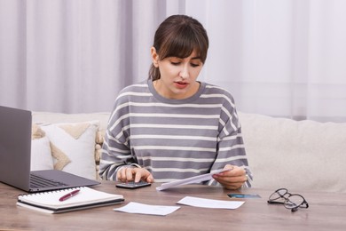 Paying bills. Woman with different invoices and calculator at wooden table indoors