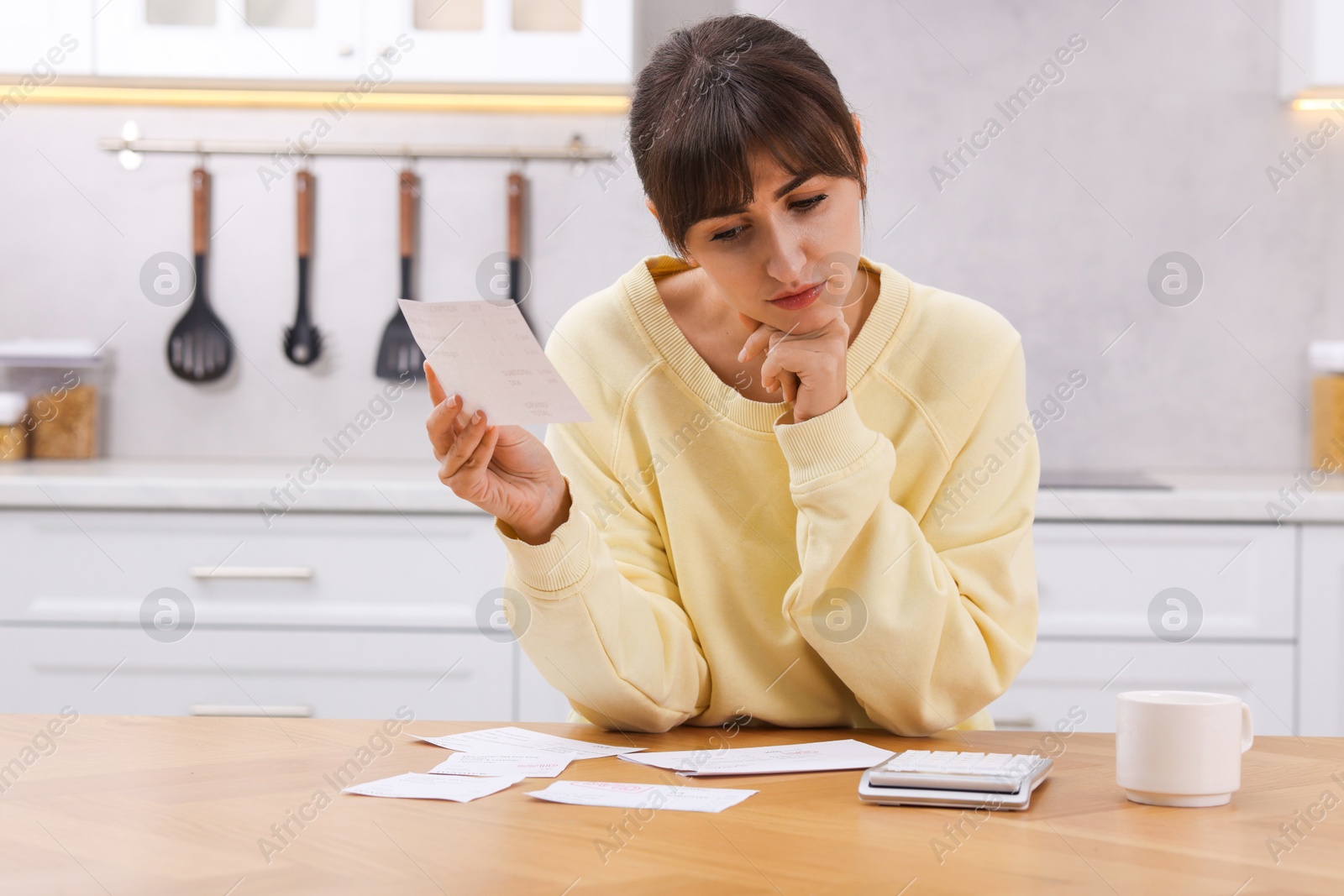 Photo of Paying bills. Upset woman with different invoices and calculator at wooden table indoors