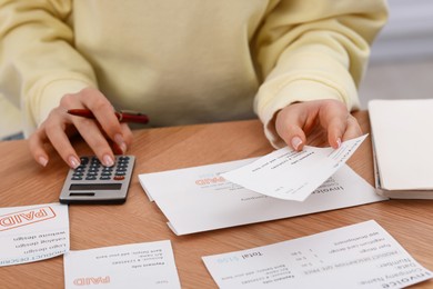 Photo of Paying bills. Woman with different invoices and calculator at wooden table indoors, closeup