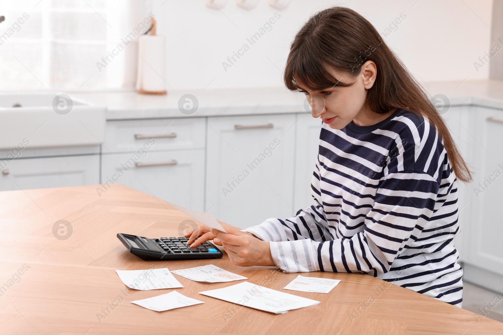 Photo of Paying bills. Woman with different invoices and calculator at wooden table indoors, space for text