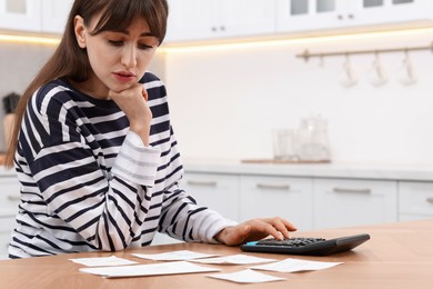 Photo of Paying bills. Woman with different invoices and calculator at wooden table indoors, space for text