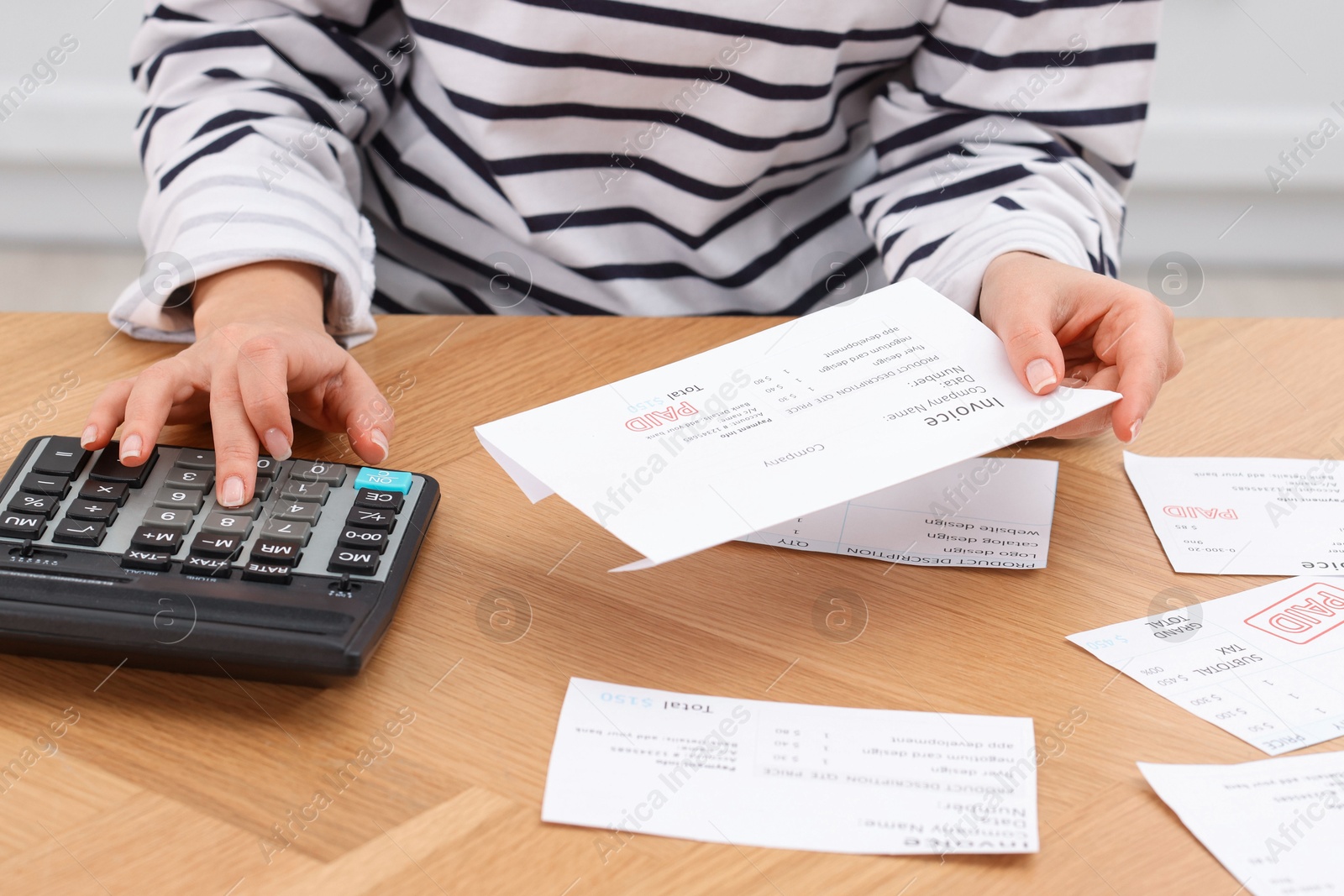 Photo of Paying bills. Woman with different invoices and calculator at wooden table indoors, closeup