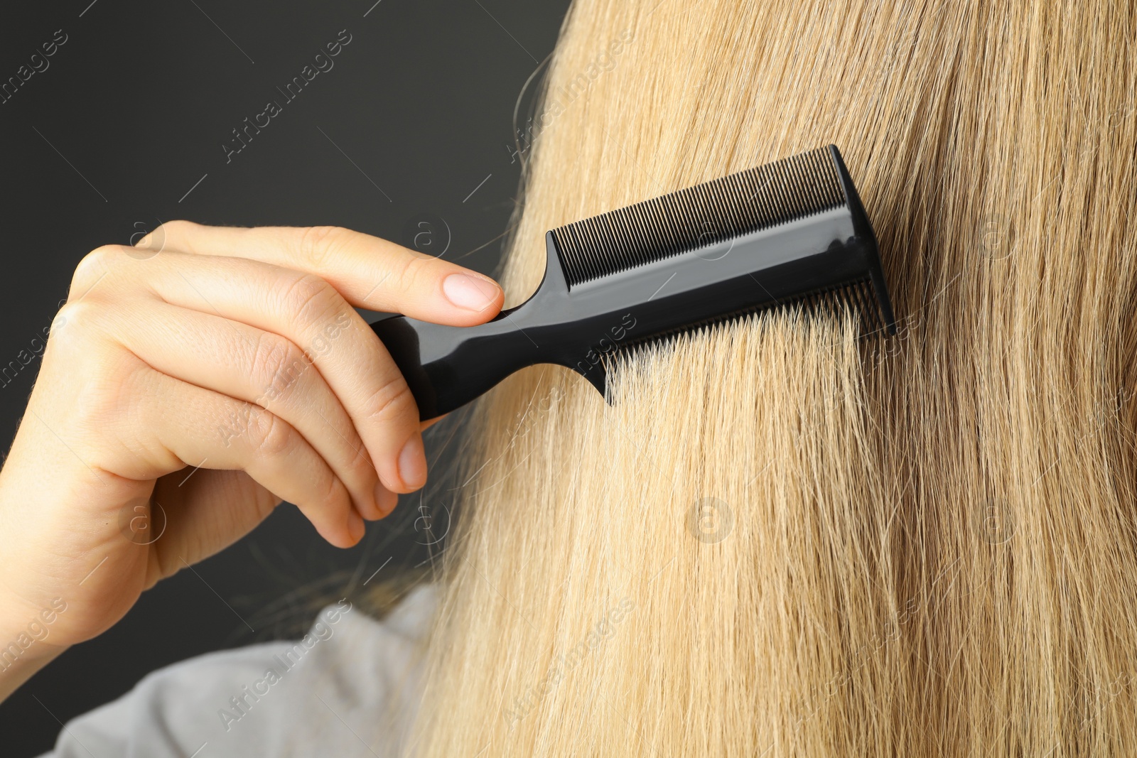 Photo of Woman brushing hair with plastic comb on grey background, closeup