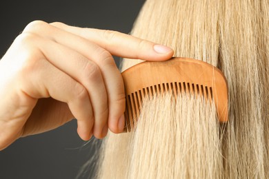 Photo of Woman brushing hair with wooden comb on grey background, closeup