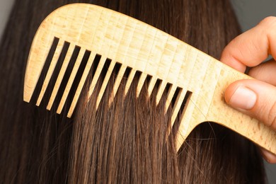 Photo of Woman brushing hair with wooden comb on grey background, closeup