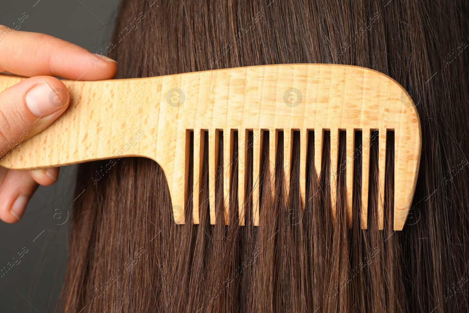 Photo of Woman brushing hair with wooden comb on grey background, closeup