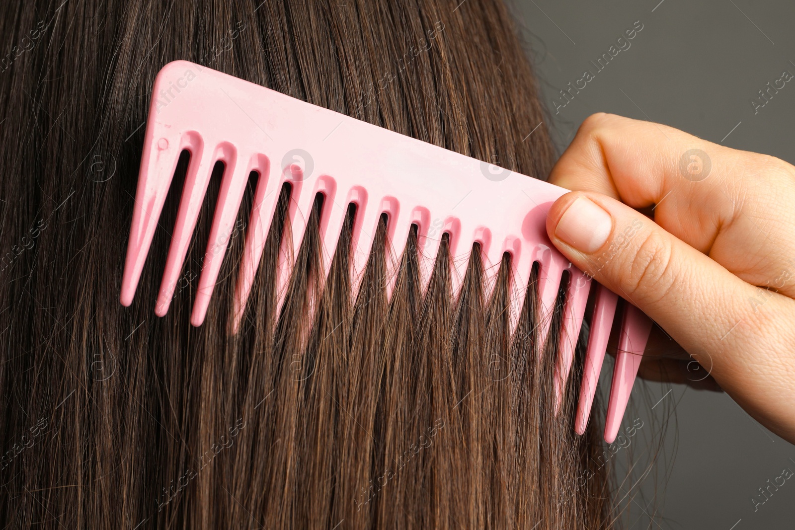 Photo of Woman brushing hair with plastic comb on grey background, closeup