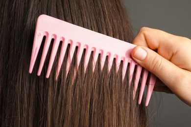 Photo of Woman brushing hair with plastic comb on grey background, closeup