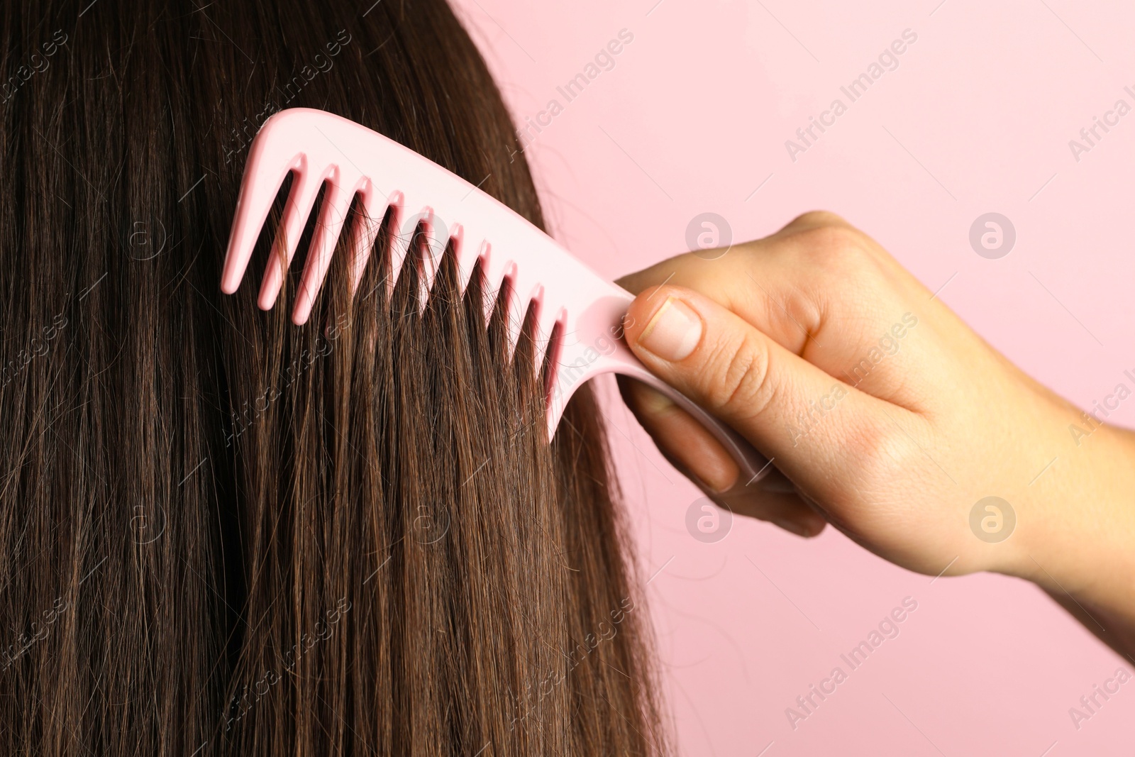 Photo of Woman brushing hair with plastic comb on pink background, closeup