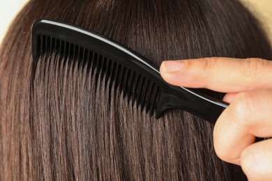 Photo of Woman brushing hair with plastic comb, closeup