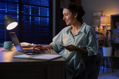 Photo of Woman with smartphone working on laptop at desk in home office