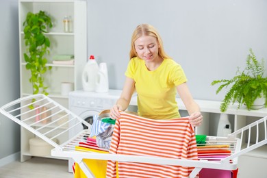 Photo of Beautiful woman hanging fresh clean laundry on drying rack at home