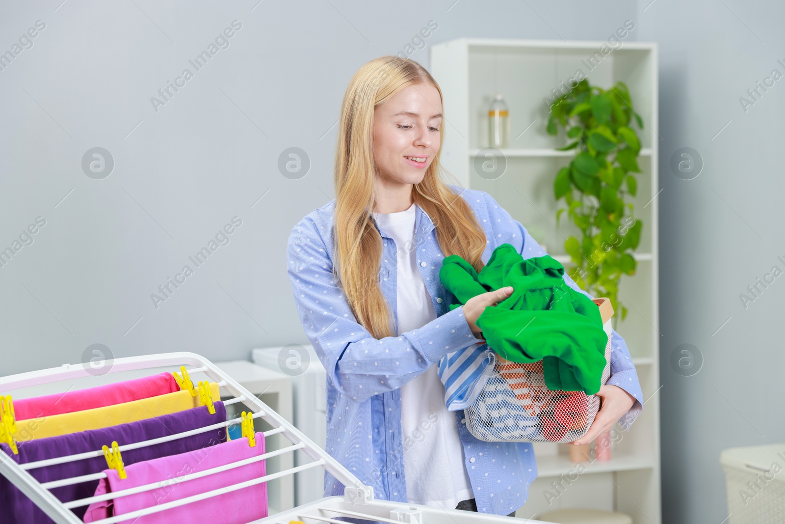 Photo of Beautiful woman hanging fresh clean laundry on drying rack at home