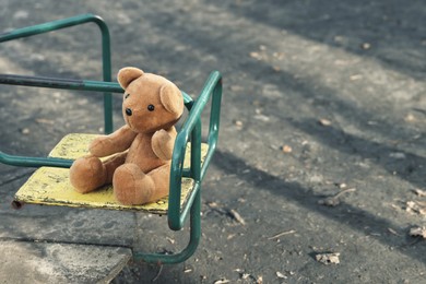 Photo of Lost brown teddy bear on merry-go-round outdoors, closeup. Space for text