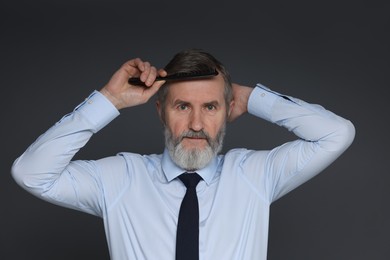 Photo of Handsome man combing his hair on dark grey background