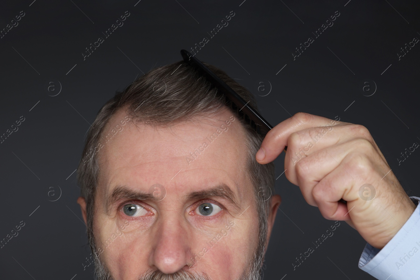 Photo of Man combing his hair on dark grey background, closeup