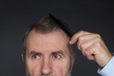 Photo of Man combing his hair on dark grey background, closeup