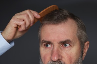 Photo of Man combing his hair on dark grey background, closeup