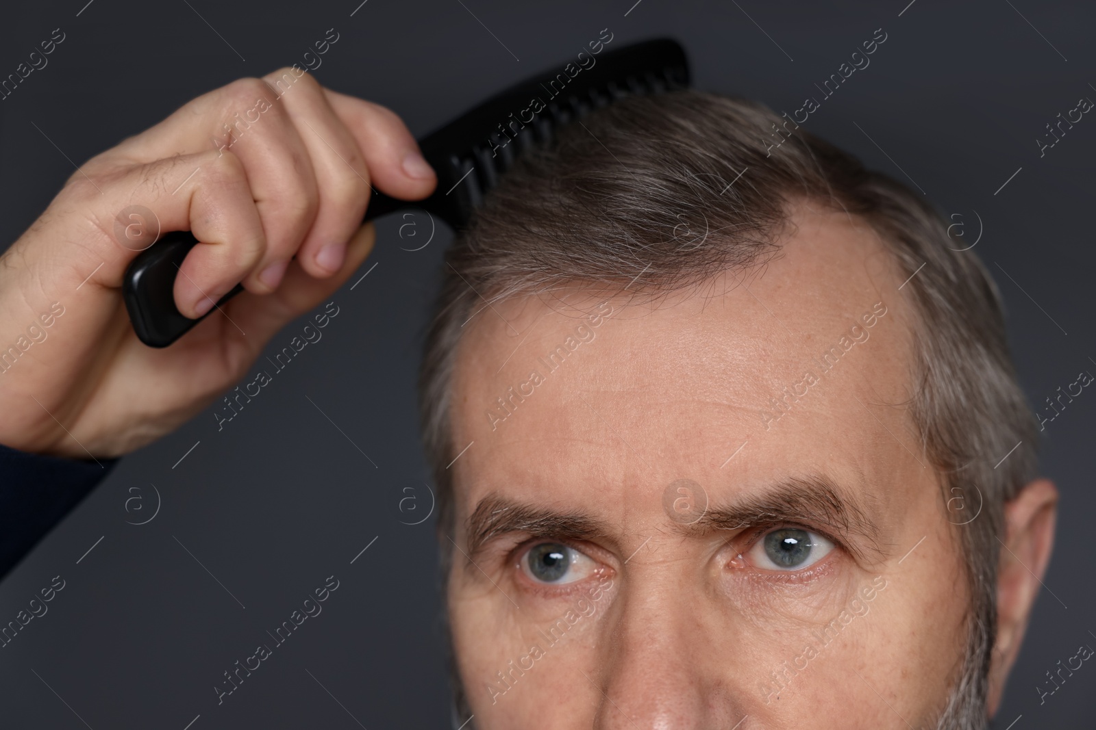 Photo of Man combing his hair on dark grey background, closeup